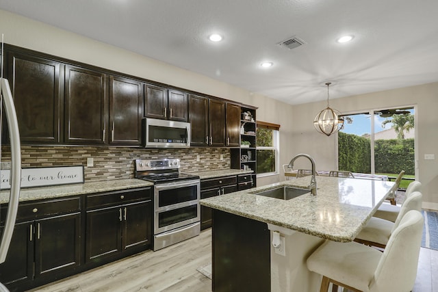 244 Behring Way, Jupiter, FL 33458 - kitchen featuring stainless steel appliances, light wood-type flooring, tasteful backsplash, a center island with sink, and light stone counters