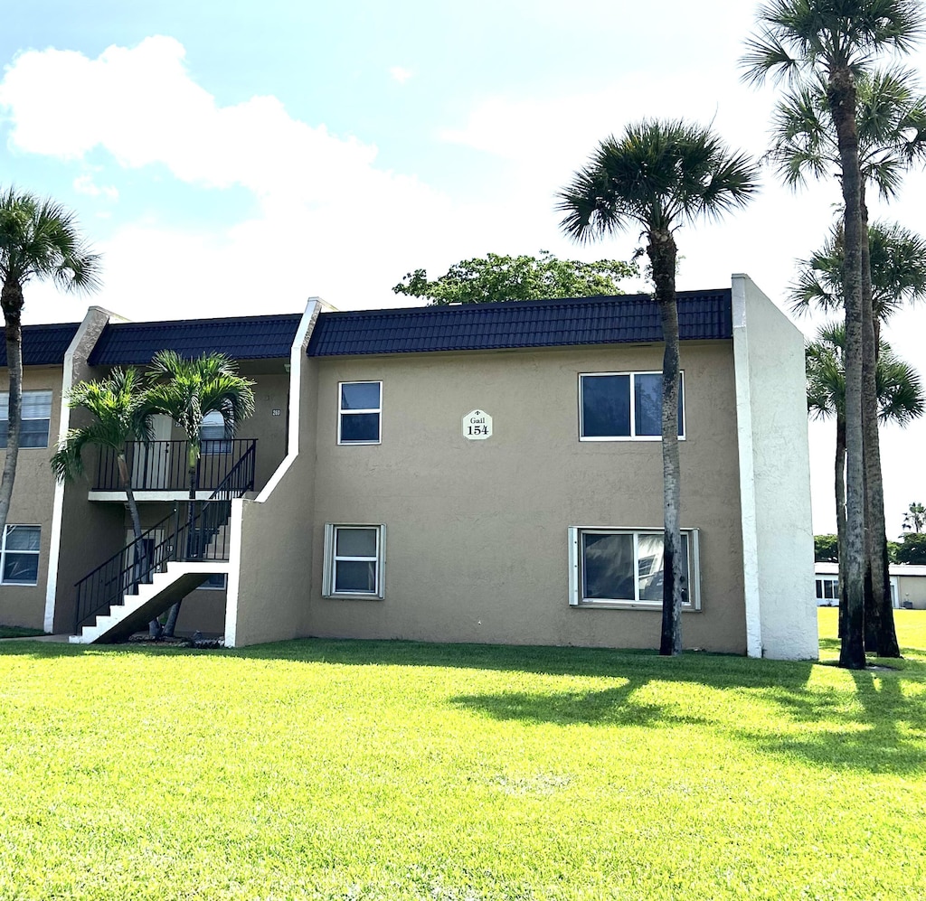 154 Lake Meryl Dr Unit 159, West Palm Beach, FL 33411 - back of house featuring stairs, stucco siding, and a yard