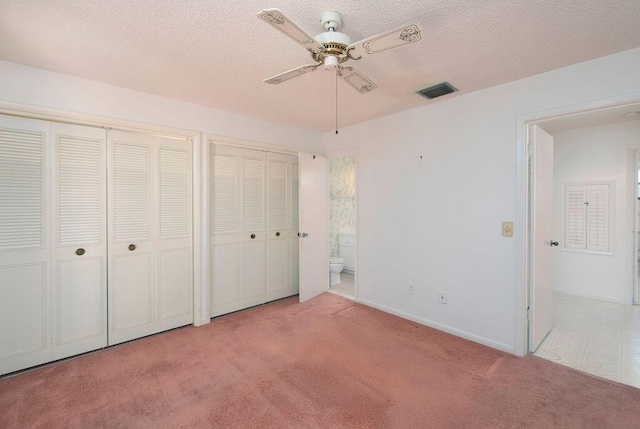 325 SE Bayview Ter, Port Saint Lucie, FL 34983 - unfurnished bedroom with light colored carpet, two closets, a textured ceiling, ensuite bath, and a ceiling fan