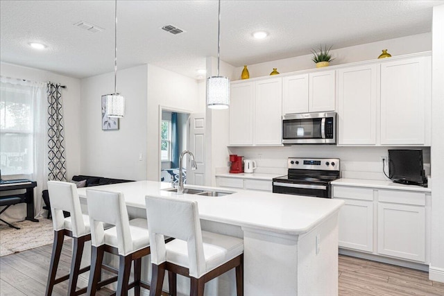 5371 NW Almond Ave, Port Saint Lucie, FL 34986 - kitchen with stainless steel microwave, range with electric cooktop, light wood-style floors, a kitchen island with sink, and a textured ceiling
