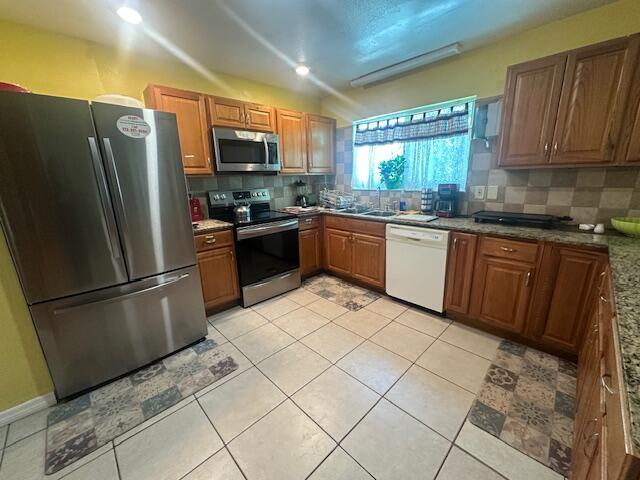 1910 SE Rainier Rd, Port Saint Lucie, FL 34952 - kitchen with appliances with stainless steel finishes, backsplash, brown cabinetry, and light tile patterned floors