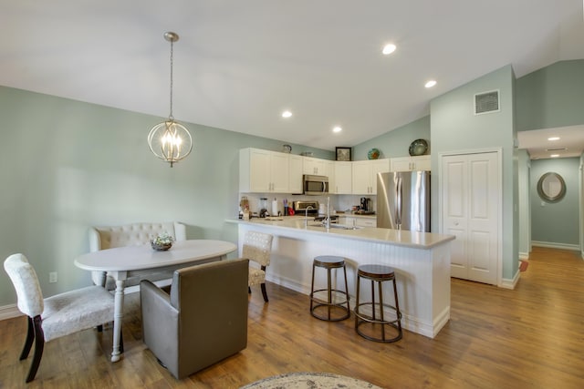 9155 SE Athena St, Hobe Sound, FL 33455 - kitchen featuring stainless steel appliances, white cabinets, a kitchen breakfast bar, light countertops, and wood finished floors