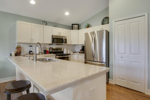 9155 SE Athena St, Hobe Sound, FL 33455 - kitchen with stainless steel appliances, a peninsula, white cabinetry, light stone counters, and light wood-style flooring