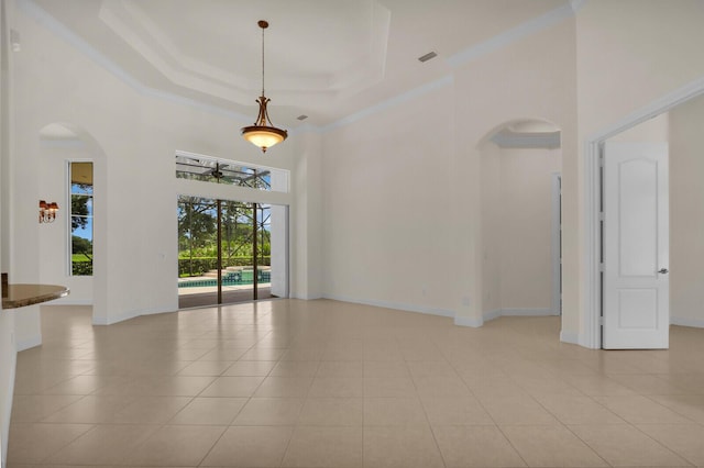 8732 Bally Bunion Rd, Port Saint Lucie, FL 34986 - empty room featuring a high ceiling, light tile patterned flooring, arched walkways, a tray ceiling, and ornamental molding