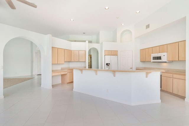 6025 Fountain Palm Dr, Jupiter, FL 33458 - kitchen with white appliances, light brown cabinets, a breakfast bar, a high ceiling, and light countertops