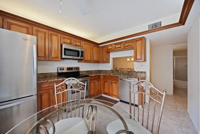 15378 Lakes Of Delray Blvd Unit 15, Delray Beach, FL 33484 - kitchen featuring appliances with stainless steel finishes, brown cabinets, light tile patterned floors, dark stone countertops, and ceiling fan