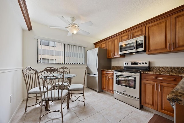 15378 Lakes Of Delray Blvd Unit 15, Delray Beach, FL 33484 - kitchen with appliances with stainless steel finishes, brown cabinetry, a ceiling fan, dark stone countertops, and light tile patterned floors