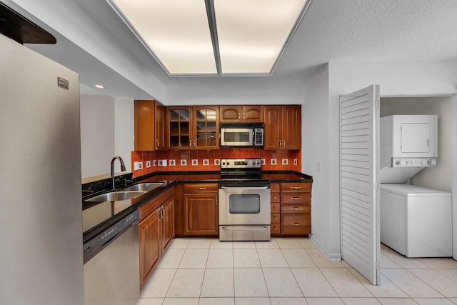 14623 Bonaire Blvd Unit 203, Delray Beach, FL 33446 - kitchen featuring appliances with stainless steel finishes, stacked washing machine and dryer, brown cabinetry, and tasteful backsplash