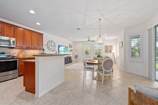 709 SW Sun Cir, Palm City, FL 34990 - kitchen with appliances with stainless steel finishes, recessed lighting, backsplash, brown cabinets, and a kitchen island with sink