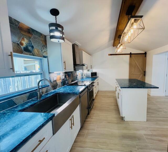 181 NE 15th Ter, Boca Raton, FL 33432 - kitchen featuring stainless steel appliances, wall chimney range hood, tasteful backsplash, a barn door, and white cabinetry