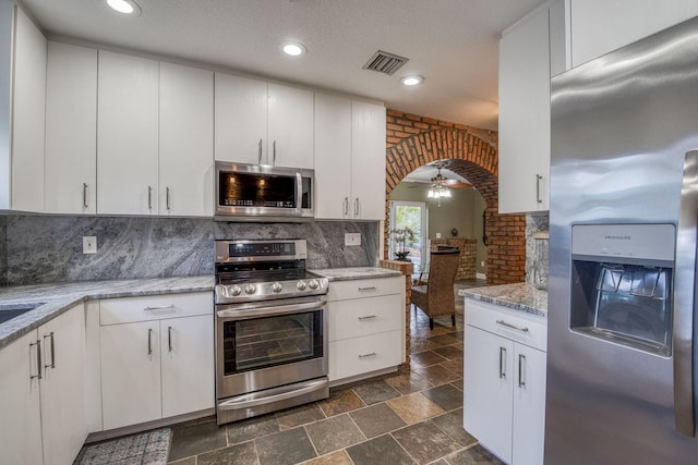 130 S Ocean Breeze, Lake Worth Beach, FL 33460 - kitchen with stainless steel appliances, arched walkways, decorative backsplash, light stone countertops, and a ceiling fan