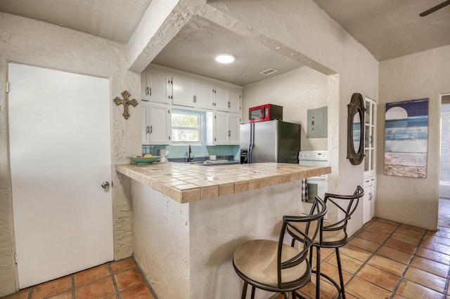 130 S Ocean Breeze, Lake Worth Beach, FL 33460 - kitchen featuring stainless steel fridge with ice dispenser, tile countertops, white cabinets, a breakfast bar, and a textured wall