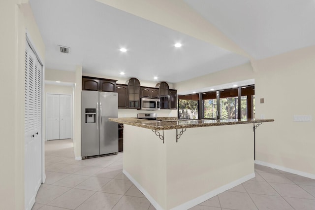 2774 SE Howell Ave, Port Saint Lucie, FL 34952 - kitchen featuring appliances with stainless steel finishes, dark brown cabinetry, a kitchen bar, light tile patterned flooring, and a kitchen island