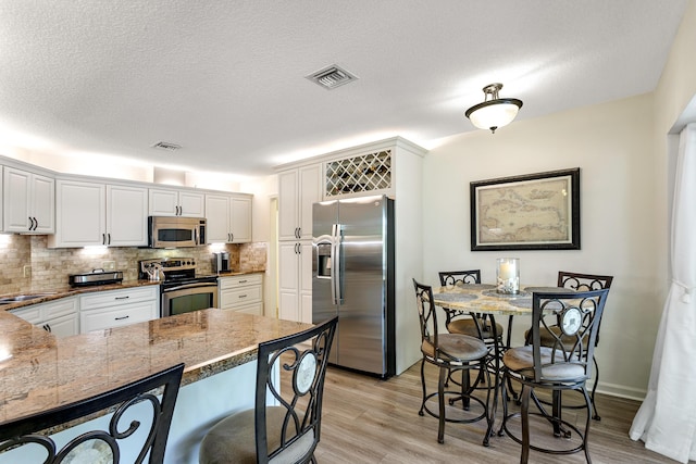 207 Jupiter Woods Dr, Jupiter, FL 33458 - kitchen with stainless steel appliances, tasteful backsplash, light wood-style floors, white cabinetry, and a peninsula