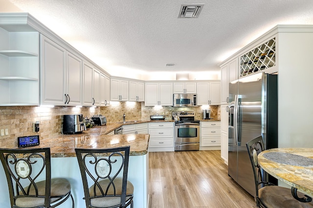 207 Jupiter Woods Dr, Jupiter, FL 33458 - kitchen featuring appliances with stainless steel finishes, a peninsula, light wood-style floors, dark stone countertops, and white cabinetry