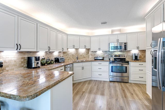 207 Jupiter Woods Dr, Jupiter, FL 33458 - kitchen featuring appliances with stainless steel finishes, a peninsula, a textured ceiling, white cabinets, and light wood finished floors