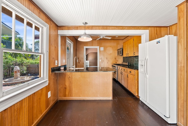 909 N L St, Lake Worth Beach, FL 33460 - kitchen with stainless steel appliances, wood walls, brown cabinetry, a ceiling fan, and dark countertops