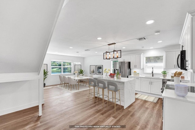 4110 NW 10th St, Delray Beach, FL 33445 - kitchen with stainless steel fridge with ice dispenser, white cabinetry, a kitchen island, a breakfast bar, and light wood-style flooring
