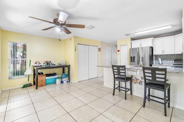 841 Summit Lake Dr, West Palm Beach, FL 33406 - kitchen with stainless steel fridge with ice dispenser, a breakfast bar, white cabinetry, light stone countertops, and ceiling fan