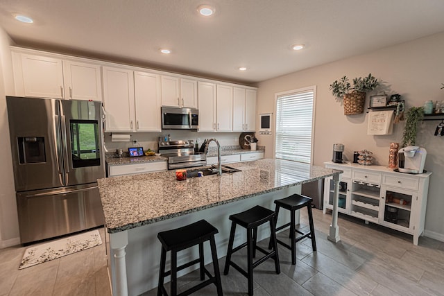 10782 SW Vasari Way, Port Saint Lucie, FL 34987 - kitchen with appliances with stainless steel finishes, white cabinets, light stone countertops, a kitchen breakfast bar, and an island with sink
