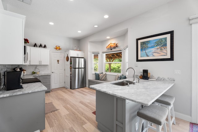 2051 SW Pruitt St, Port Saint Lucie, FL 34953 - kitchen featuring freestanding refrigerator, a peninsula, light wood-style flooring, a breakfast bar, and decorative backsplash