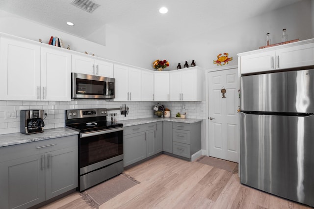 2051 SW Pruitt St, Port Saint Lucie, FL 34953 - kitchen with appliances with stainless steel finishes, gray cabinetry, decorative backsplash, light wood finished floors, and white cabinetry