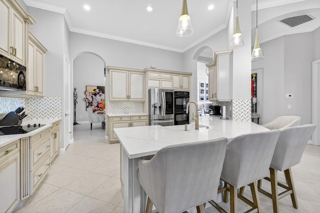 8168 Valhalla Dr, Delray Beach, FL 33446 - kitchen with cream cabinets, arched walkways, black appliances, tasteful backsplash, and a breakfast bar area