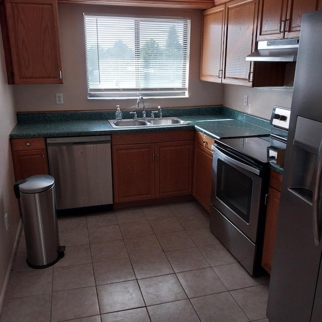 2482 SE Floresta Dr, Port Saint Lucie, FL 34984 - kitchen featuring stainless steel appliances, under cabinet range hood, dark countertops, light tile patterned floors, and brown cabinets