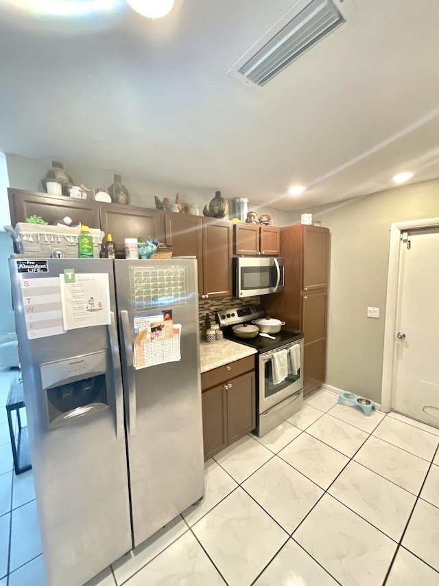 409 NE Oleander Ave, Port Saint Lucie, FL 34952 - kitchen with stainless steel appliances, light tile patterned floors, light countertops, and brown cabinets