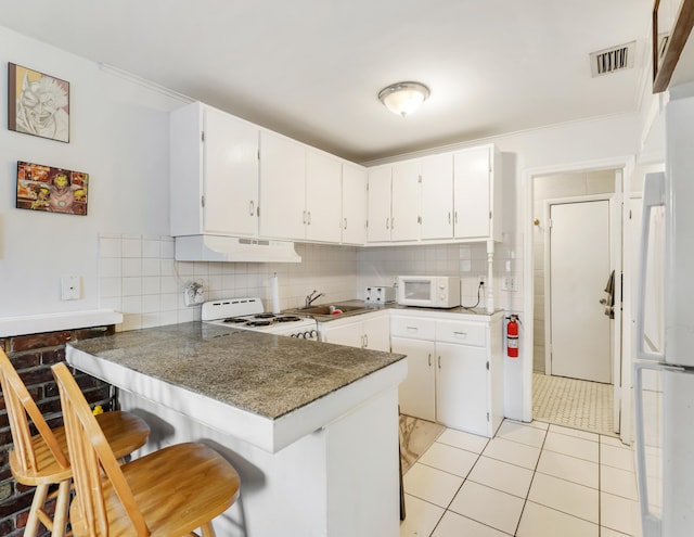 918 Grace Ave, Lake Worth, FL 33461 - kitchen with white microwave, stove, under cabinet range hood, a peninsula, and decorative backsplash