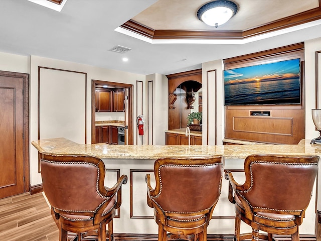 2 Renaissance Way Unit 302, Boynton Beach, FL 33426 - kitchen featuring a raised ceiling, light wood-type flooring, light stone counters, a breakfast bar, and ornamental molding