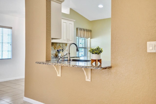8140 Palm Gate Dr, Boynton Beach, FL 33436 - kitchen featuring a breakfast bar, light stone countertops, backsplash, white cabinetry, and light tile patterned flooring