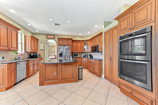 7486 Greenville Cir, Lake Worth, FL 33467 - kitchen featuring appliances with stainless steel finishes, arched walkways, light tile patterned floors, decorative backsplash, and brown cabinets