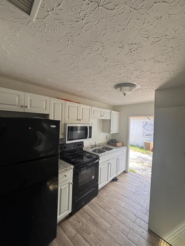 503 N 25th St, Fort Pierce, FL 34947 - kitchen featuring black appliances, white cabinetry, light wood-type flooring, light countertops, and a textured ceiling