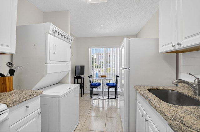13984 Via Flora Unit B, Delray Beach, FL 33484 - kitchen featuring stacked washer and clothes dryer, white cabinetry, light stone countertops, a textured ceiling, and light tile patterned floors