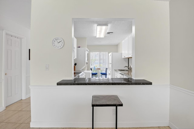 13984 Via Flora Unit B, Delray Beach, FL 33484 - kitchen with freestanding refrigerator, white cabinets, light tile patterned floors, a peninsula, and a textured ceiling