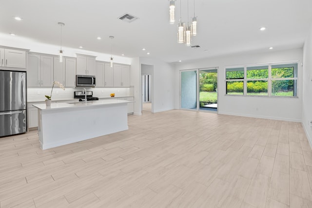 11687 SW Viridian Blvd, Port Saint Lucie, FL 34987 - kitchen featuring appliances with stainless steel finishes, a kitchen island with sink, light countertops, open floor plan, and backsplash