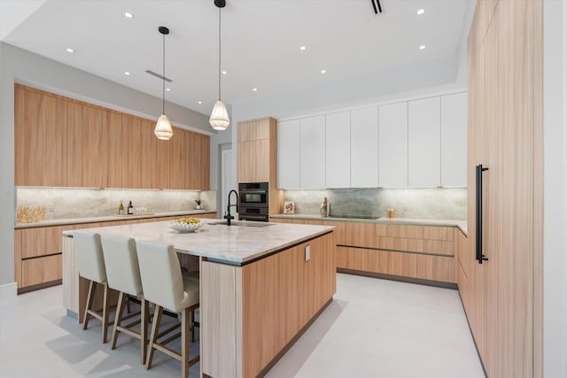 2265 NE 30th Ct, Lighthouse Point, FL 33064 - kitchen with modern cabinets, an island with sink, tasteful backsplash, a breakfast bar area, and light stone counters
