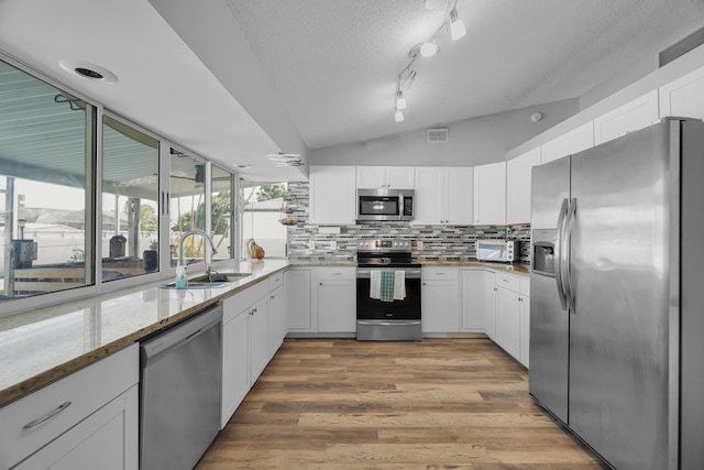 356 SW Grimaldo Ter, Port Saint Lucie, FL 34984 - kitchen with appliances with stainless steel finishes, light stone counters, white cabinetry, vaulted ceiling, and a textured ceiling