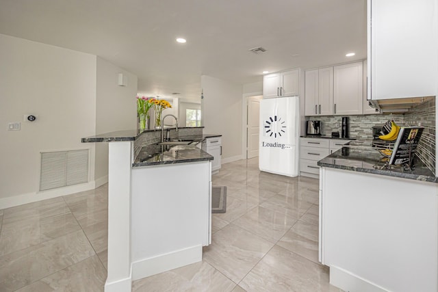 1518 Lee Ct, Lake Worth, FL 33461 - kitchen with white refrigerator, backsplash, light marble finish flooring, dark stone countertops, and white cabinetry