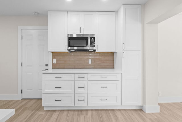 1522 Lance Rd, Jupiter, FL 33469 - kitchen with stainless steel microwave, light countertops, light wood-style flooring, white cabinets, and decorative backsplash