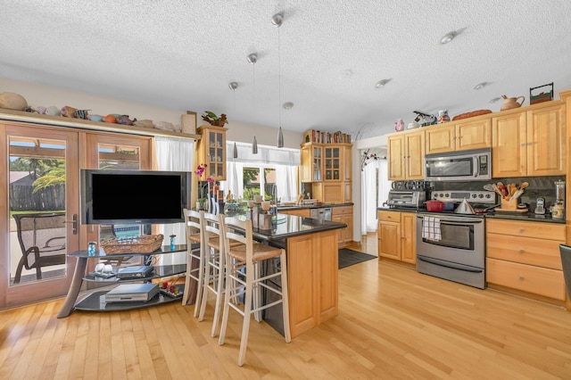 9070 NW 16th St, Plantation, FL 33322 - kitchen featuring appliances with stainless steel finishes, dark countertops, a textured ceiling, light wood-style floors, and glass insert cabinets