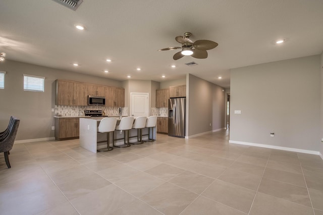 1878 NE Ocean Dunes Dr, Jensen Beach, FL 34957 - kitchen featuring appliances with stainless steel finishes, backsplash, a breakfast bar area, a kitchen island with sink, and ceiling fan
