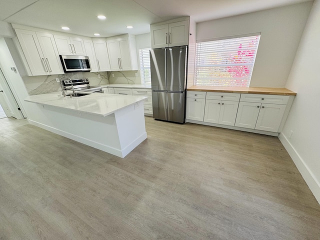 970 Normandy U, Delray Beach, FL 33484 - kitchen featuring stainless steel appliances, light wood-type flooring, white cabinetry, a peninsula, and backsplash