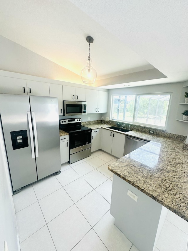 6455 NW Foxglove St, Port Saint Lucie, FL 34986 - kitchen with stainless steel appliances, light stone counters, pendant lighting, white cabinetry, and a tray ceiling