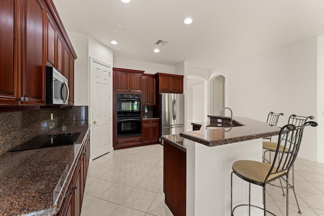879 SW Pebble Ln, Palm City, FL 34990 - kitchen featuring black appliances, dark brown cabinets, light tile patterned flooring, a breakfast bar area, and backsplash