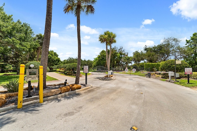 879 SW Pebble Ln, Palm City, FL 34990 - view of asphalt road featuring curbs, a gate, a gated entry, traffic signs, and view of wooded area