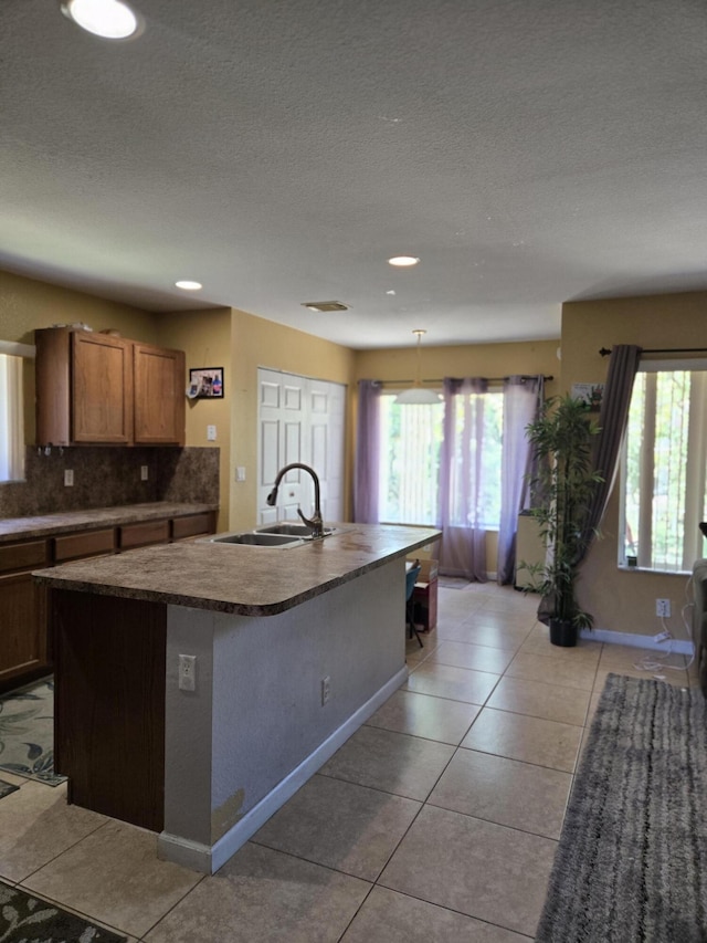 2137 Little Torch St, Riviera Beach, FL 33407 - kitchen with decorative backsplash, dark countertops, a kitchen island with sink, light tile patterned floors, and a textured ceiling