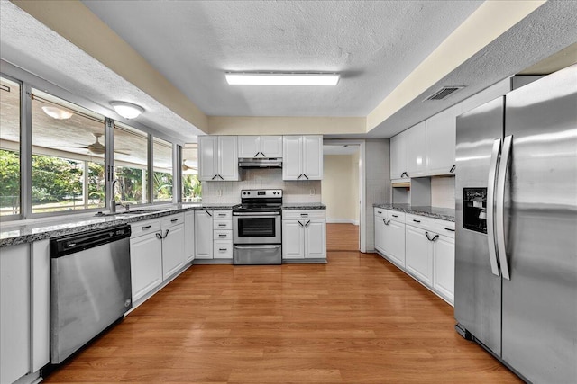 11061 NW 45th St, Coral Springs, FL 33065 - kitchen featuring stainless steel appliances, white cabinetry, backsplash, light wood-style floors, and a textured ceiling