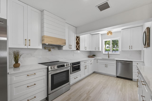 131 Cruiser Rd S, North Palm Beach, FL 33408 - kitchen featuring stainless steel appliances, white cabinets, decorative backsplash, and light wood-type flooring